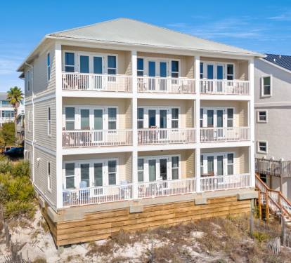 Coastal vacation home featuring multiple balconies and bright windows, situated steps from sandy beaches with natural dune vegetation.