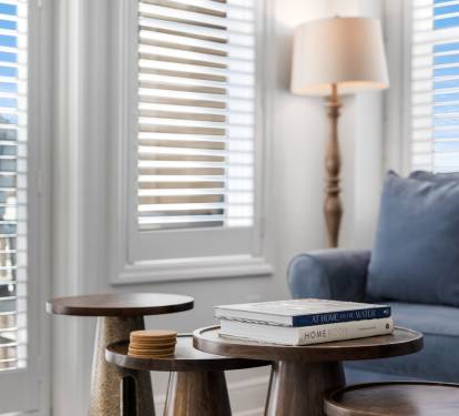Sink into your cozy living space with plush blue seating, natural light filtering through elegant blinds, and thoughtful touches like curated books awaiting your leisurely moments.