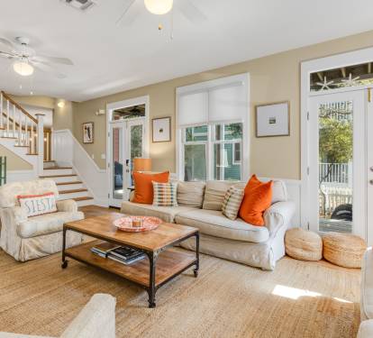 Relax in your bright, airy living room with vibrant orange accents and comfortable seating that opens to outdoor spaces.