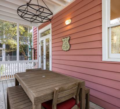Relax on your charming covered porch with rustic dining table, perfect for morning coffee or evening meals in the peaceful neighborhood setting.