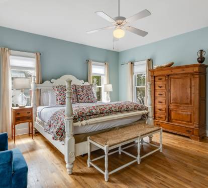 Unwind in your elegant bedroom featuring a plush four-poster bed, rich hardwood floors, and calming blue walls that create a peaceful retreat.