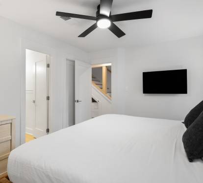 Drift off in your serene bedroom with crisp linens, modern ceiling fan, and wall-mounted TV for relaxation.