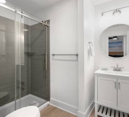 Your private bathroom features a spacious glass shower, elegant vanity, and coastal artwork that creates a spa-like retreat.