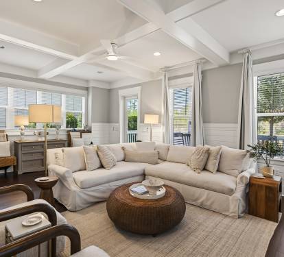 Relax in your elegant living room featuring plush sectional seating, coffered ceilings, and abundant natural light through plantation shutters.