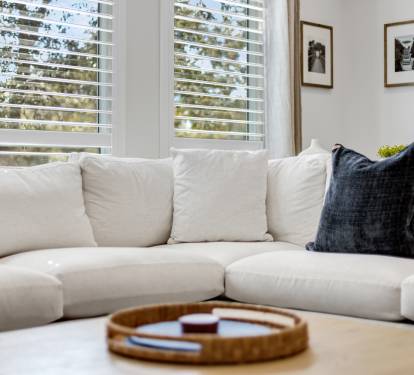 Sink into this plush white sectional sofa where natural light filters through plantation shutters, creating your perfect afternoon retreat.
