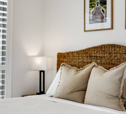Sink into this beautifully appointed bed with its woven headboard and plush pillows, where natural light filters through blinds creating your perfect retreat.