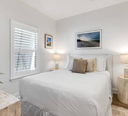 Relax in your serene bedroom featuring coastal artwork, soft lighting, and crisp white linens for the perfect night's sleep.