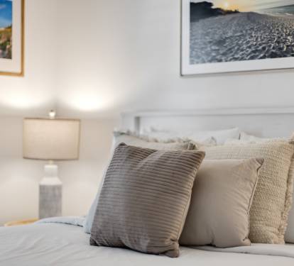 Sink into plush pillows and soft linens in your serene bedroom retreat, where coastal artwork and warm lighting create the perfect ambiance for restful nights.