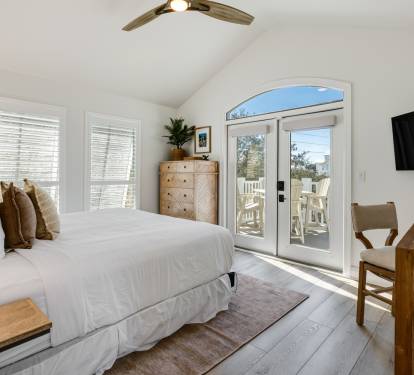 Your peaceful bedroom retreat features crisp white linens, warm wood accents, and French doors opening to your private balcony.