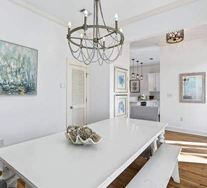 Gather around your elegant dining table beneath the stunning chandelier, where coastal artwork and warm hardwood floors create the perfect setting for memorable meals.