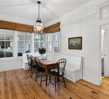 Your charming dining nook features rustic wood floors, classic Windsor chairs, and warm natural light streaming through bamboo shades.