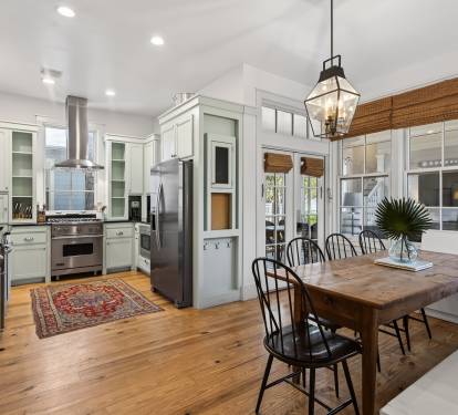 Gather around the rustic dining table in this bright, chef-inspired kitchen where warm wood floors and charming lantern lighting create the perfect atmosphere for your meals.