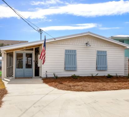 Charming beachside cottage with blue shutters and welcoming front porch in a quiet coastal neighborhood.
