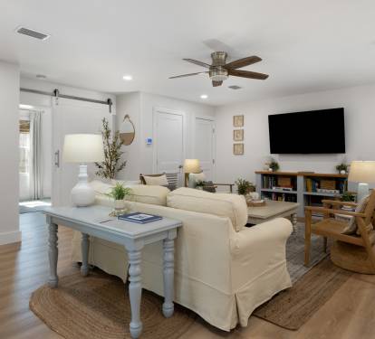 Unwind in your bright, modern living room with cozy seating, entertainment center, and coastal touches throughout.