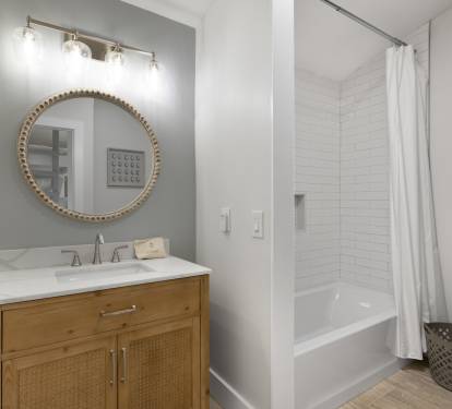 Step into your stylish bathroom featuring a warm wood vanity, elegant round mirror, and refreshing tub-shower combo for unwinding after adventures.