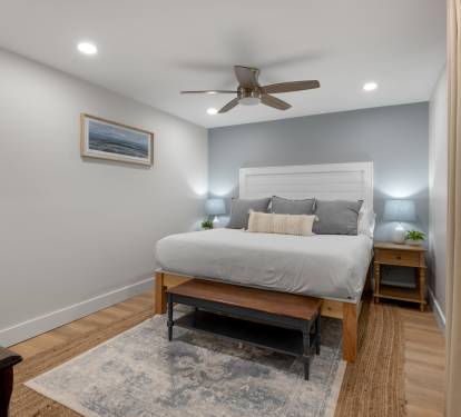 Relax in your cozy bedroom with comfortable bedding, peaceful coastal artwork, and gentle ceiling fan creating the perfect retreat.