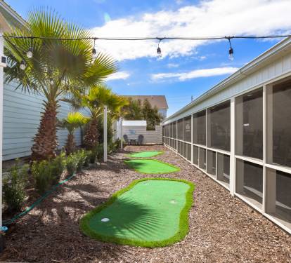 Your private mini golf course awaits under swaying palms and string lights, creating the perfect evening entertainment in your tropical backyard oasis.