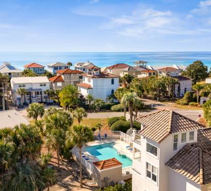 Elevated aerial view showcases a coastal neighborhood with colorful beachfront homes and palm-lined streets near pristine turquoise waters.