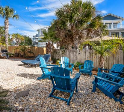 Relax in your private backyard oasis with vibrant blue Adirondack chairs, tropical palms, and string lights for magical evenings under the stars.