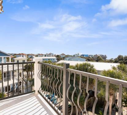 Private balcony with decorative railings overlooking coastal neighborhood homes and palm trees under bright blue skies.