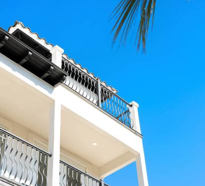 Beautiful white villa with elegant balconies and Mediterranean-style railings under bright blue skies and palm trees.