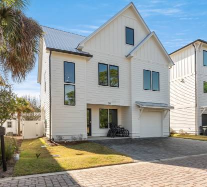 Modern coastal home featuring light-colored siding and metal roof, nestled among palm trees in a charming neighborhood setting.