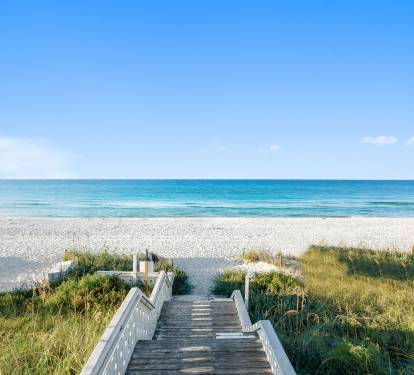 Pristine sandy beach meets crystal-clear waters, accessed by a charming wooden walkway through natural dunes.