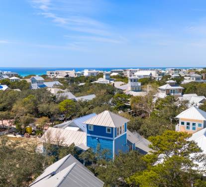 Aerial view showcases the scenic coastal community with charming beach houses nestled among lush trees, just steps from pristine blue waters.