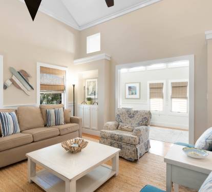 Relax in your bright, airy living room with plush seating and coastal charm. Natural light fills the space through elegant windows.