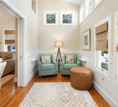 Your peaceful reading nook awaits with twin seafoam chairs, warm leather ottoman, and natural light streaming through bamboo shades.