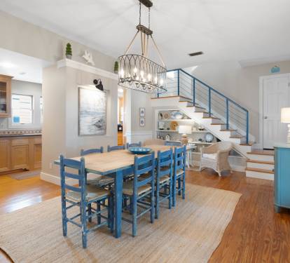 Coastal charm meets modern comfort in your open-plan living space, where blue accents and warm wood floors create the perfect backdrop for memorable meals.