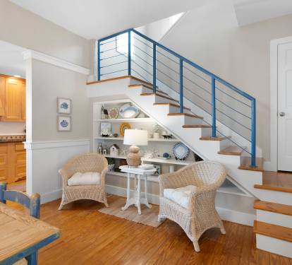 Your charming living space features nautical touches and cozy wicker seating beneath sleek stairs, perfect for morning coffee or evening relaxation.