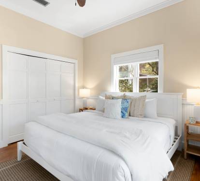 Sink into plush white linens in your peaceful retreat, where warm beige walls and crisp white wainscoting create a cozy sanctuary for restful nights.