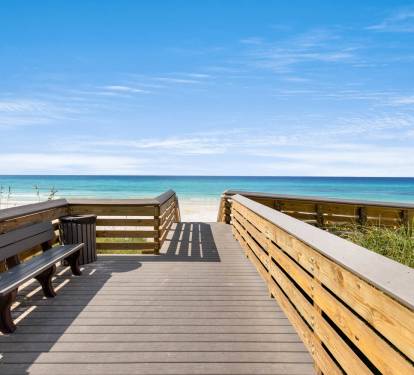 Wooden boardwalk overlooking pristine white sand beach and turquoise waters under clear blue skies.