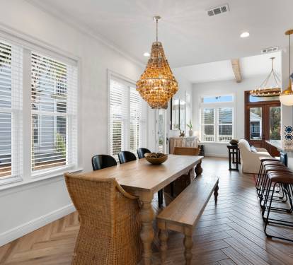 You'll love gathering around this stunning farmhouse table, bathed in natural light from oversized windows while the golden chandelier creates perfect ambiance.