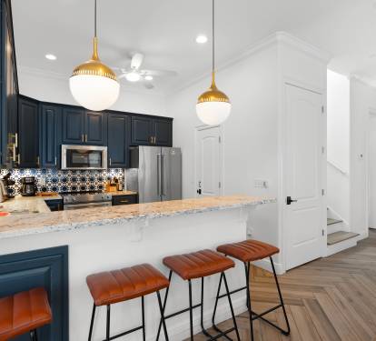 You'll love cooking in this stylish kitchen featuring navy cabinets, gold pendant lights, and a spacious marble island perfect for morning coffee.