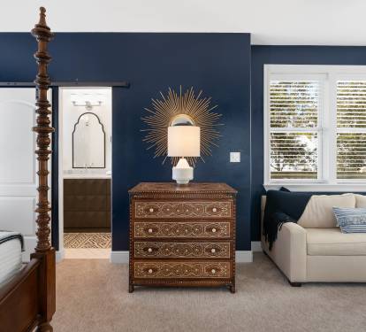 Unwind in your elegant bedroom featuring rich navy walls, a four-poster bed, and cozy seating area perfect for morning coffee.