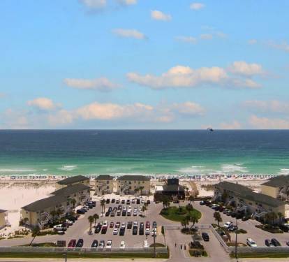 Aerial view of beachfront property complex with direct beach access and expansive parking facilities.