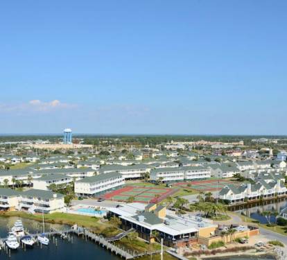Aerial view of waterfront resort complex with marina, tennis courts, pool facilities and nearby residential community.