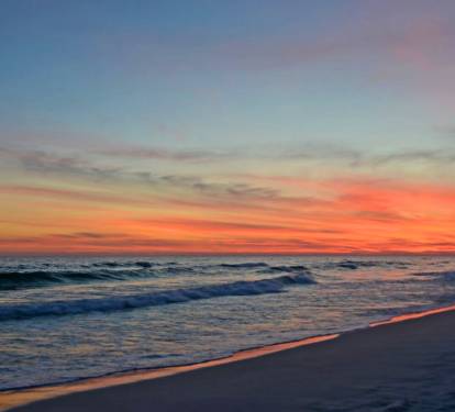 Stunning Gulf sunset with colorful skies reflecting over gentle waves and sugar-white sand, creating a serene coastal scene perfect for evening strolls and quiet moments by the water.