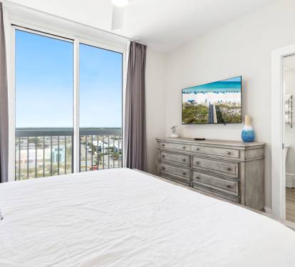Wake up to stunning ocean views from your private balcony in this bright, elegant bedroom with modern coastal furnishings and TV.
