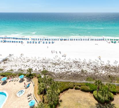 Stunning aerial view showcases pristine white sand beach with crystal-clear turquoise waters and organized beach umbrella rows stretching along the coastline.