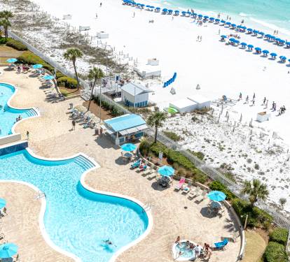 Beachfront resort with multi-level pools, white sand beach, and turquoise waters stretching to the horizon.
