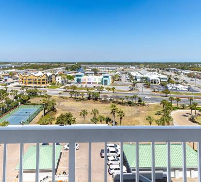 Elevated view from balcony overlooking tennis courts, palm trees, and the vibrant town center below.