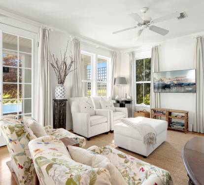 Sink into this sun-soaked living room where French doors reveal serene lake views and gentle breezes flow through your bright, coastal retreat.