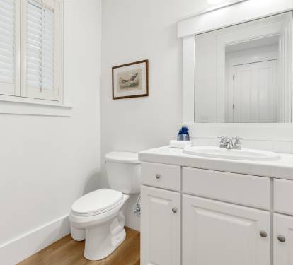 Your pristine white bathroom features warm wood floors, elegant shutters, and thoughtful touches like fluffy towels and coastal artwork.