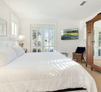 Drift off in your serene bedroom with crisp white linens, elegant plantation shutters, and an antique armoire creating the perfect coastal retreat.