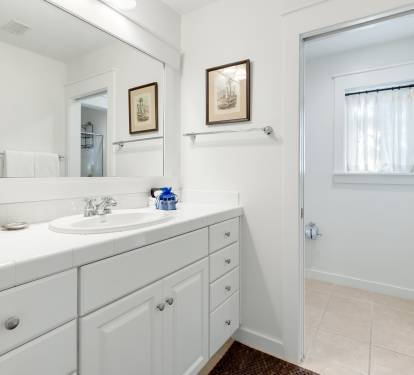 Step into your pristine bathroom featuring crisp white cabinetry, spacious vanity, and charming nautical artwork that creates a serene coastal atmosphere.