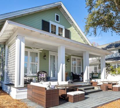 Charming green cottage with spacious covered porch featuring comfortable outdoor furniture for relaxing in the fresh air.