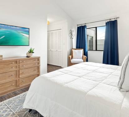Unwind in your serene bedroom with plush white bedding, coastal TV entertainment, and a cozy reading nook by the window.